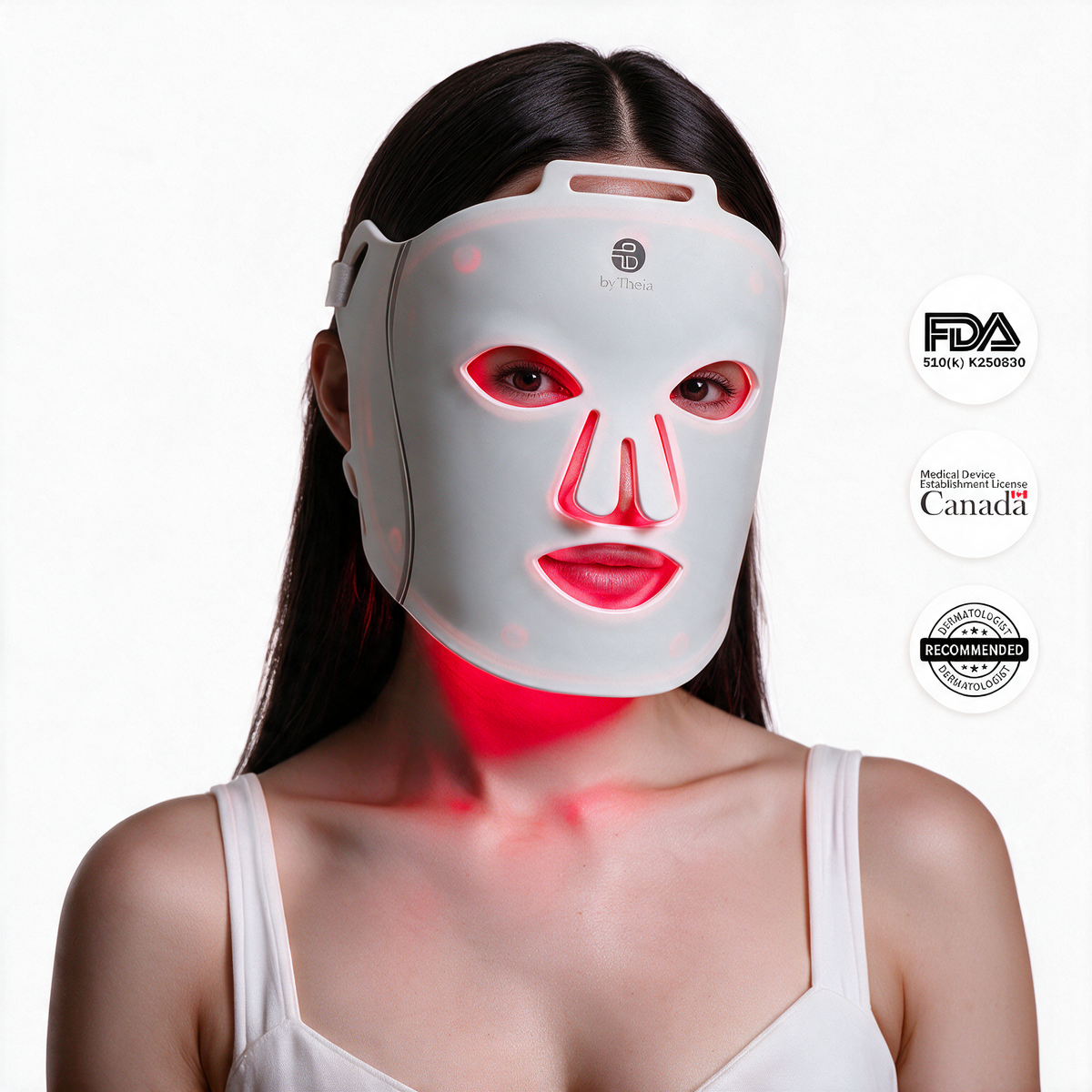 A woman wearing a byTheia LED light therapy face mask that glows red around her eyes, nose, and mouth, shown against a white background with FDA, Product Certification Canada, and Recommended seals on the right.