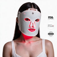A woman wearing a byTheia LED light therapy face mask that glows red around her eyes, nose, and mouth, shown against a white background with FDA, Product Certification Canada, and Recommended seals on the right.