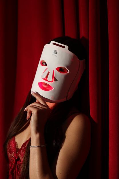 byTheia BTFM03 LED face mask held to the face in an editorial portrait against a red backdrop