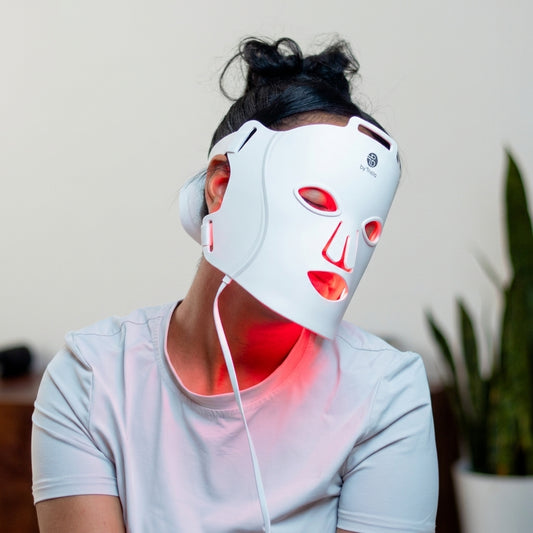 Woman holding byTheia Advanced LED Facial Mask BTFM03 with red light therapy glowing on skin — at-home skincare treatment for anti-aging and skin rejuvenation